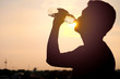 © Phawat - The silhouette of a man drinking a refreshing bottle of water on a sunset background