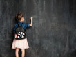© deniskomarov - Little girl with school bag near blackboard in classroom.Pupil is writing on a chalkboard in a denim shirt and a pink skirt. Education and elementary school concept.