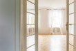 View through open glass door on an empty, bright bedroom interior with big windows, white walls and herringbone floor
