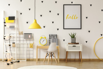 Wall Mural - Plant on cabinet next to desk and white chair in child's room interior with yellow lamp and poster. Real photo