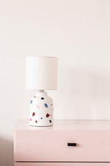 Wall Mural - Patterned lamp on pastel pink cabinet against white wall in colorful interior. Real photo