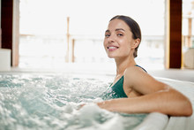 Young Woman Relaxing In Soft Waving Water While Sitting In Jacuzzi Bath At Spa Center