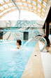 © pressmaster - Young woman enjoying water splashes on her back while standing in spa swimming-pool
