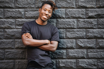 Wall Mural - Handsome smiling african american man in blank black t-shirt standing against brick wall