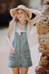 Poster - Portrait of a smiling young woman with hat leaning against rock at the beach