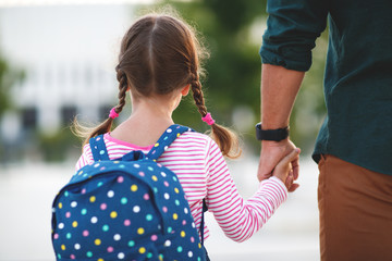 first day at school. father leads little child school girl in first grade