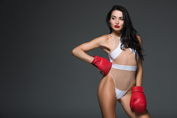 Wall Mural - seductive sportive woman in white swimwear and boxing gloves posing isolated on grey