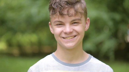 Wall Mural - Close up emotional portrait of caucasian smiling teen boy. Handsome guy. Funny cute teenager in summer park at day. Child looking at camera.