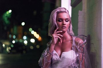 Wall Mural - sensual young woman in transparent raincoat standing on street at night under pink light