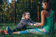 Two girls doing partner stretching yoga exercise, Paschimottanasana or seated forward bend pose, working-out outdoors