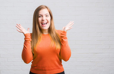 Young adult woman over white brick wall very happy and excited, winner expression celebrating victory screaming with big smile and raised hands