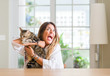 Young woman at home playing with her cat annoyed and frustrated shouting with anger, crazy and yelling with raised hand, anger concept