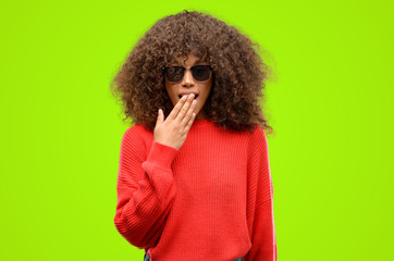 Poster - African american woman wearing sunglasses covers mouth in shock, looks shy, expressing silence and mistake concepts, scared