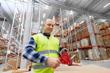 logistic business, shipment and people concept - worker in safety vest packing parcel box with scotch tape at warehouse or mail storage