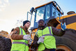 © Seventyfour - Low angle portrait of two workers, one African-American, drinking coffee and chatting standing next to heavy industrial truck on worksite