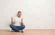 © Krakenimages.com - Young caucasian man sitting on the floor over white brick wall very happy and excited doing winner gesture with arms raised, smiling and screaming for success. Celebration concept.