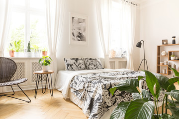 Leaf motif linen on a big bed in a modern bedroom interior with windows in a back wall. Real photo.