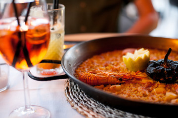 close-up of delicious seafood valencia paella with king prawns, rice with spices in pan and Glass of aperol spritz cocktail long drink, evening meal, dinner