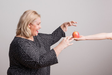 A female hand giving an apple to an attractive overweight woman in studio.