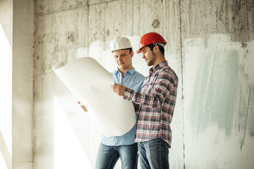 talented, creative engineer is showing the plan of object to a client in the house which is under construction. side view photo. copyspace