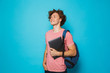 Image of attractive youngster guy with curly hair wearing casual clothing and backpack holding laptop, isolated over blue background