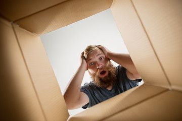 The surprised man unpacking, opening carton box and looking inside. The package, delivery, surprise, gift lifestyle concept. Human emotions and facial expressions concepts