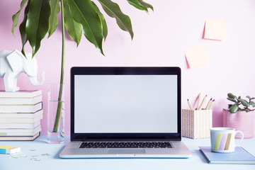 Stylish and creative desk with laptop mock up screen, tropical leaf, office accessories and memo stick. Pink background wall. Design home office interior. 