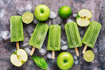 Green popsicles on a wooden background. Frozen juice on a stick, green apple, lime. Flat lay, top view