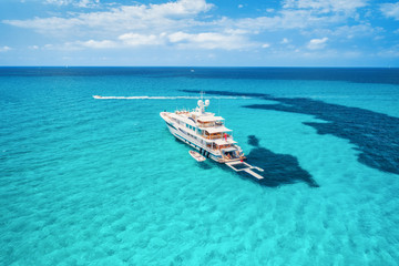 Yacht on the azure seashore in balearic islands. Aerial view of floating boat with people in transparent sea at sunny day in summer. Top view from drone. Seascape with luxury yachts in motion in bay
