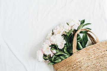Wall Mural - Straw bag with white peony flowers on white background. Flat lay, top view summer floral concept.