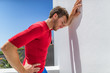 Tired athlete runner man exhausted leaning on wall of fatigue breathing hard after difficult exercise. Fitnes person sweating of sun stroke, migraine, heat exhaustion muscle back pain or cramps.