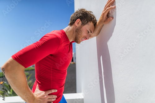Foto Tired athlete runner man exhausted leaning on wall of fatigue breathing hard after difficult exercise