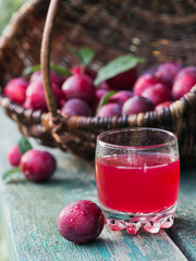 Wall Mural - A glass of berry drink and fresh plums with leaves on rustic wooden table background.