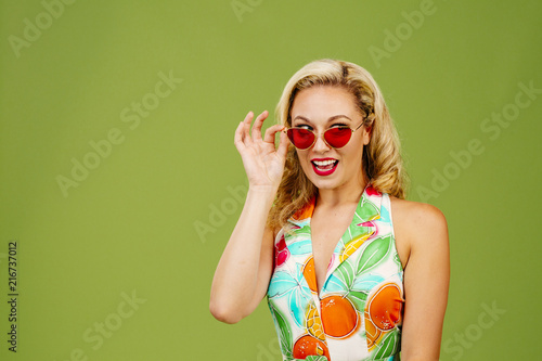 Fotografering Beautiful blonde peeking from under sunglasses, isolated on green studio backgro