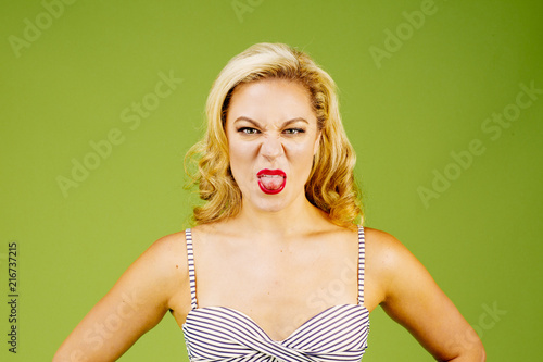 Fényképezés  Woman in striped bikini showing her tongue to camera, isolated on green studio b
