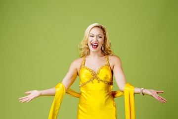 Wall Mural - A very excited  blonde  in yellow evening gown with arms out, isolated on green studio background