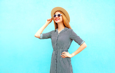 Wall Mural - Fashion smiling woman model poses in a striped dress, straw hat on blue background