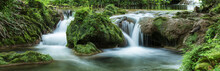 Panoramic View Of Small Waterfalls Streaming Into Small Pond In Green Forest in Long Exposure