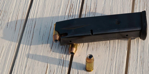 A loaded black pistol magazine on a wooden table casting it's shadow along with two 40 caliber hollow point bullets