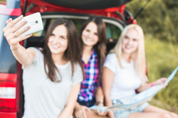 Sticker - Three young women with suitcases on a trip by car. They sit in the back of the car, they look at the map, resting after a long drive and having fun. Hitchhiking and car trips with friends