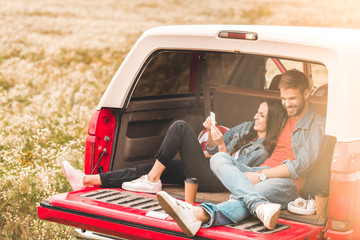 Wall Mural - beautiful young couple using smartphone while relaxing in car trunk