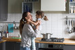 © fizkes - Smiling loving single mother holding cute little child daughter having fun together, happy family of young caring mom and excited kid girl laughing playing at home while cooking in the kitchen