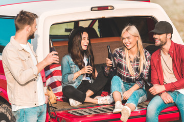 Wall Mural - group of young people drinking beer and chatting while sitting in car trunk on nature