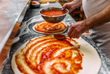 Chef baker making pizza at the kitchen. Adding tomato sauce on a pizza dough.