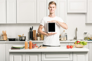 Wall Mural - handsome young man holding tablet with blank screen in kitchen