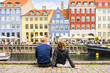 Tourists enjoying the scenic summer view of Nyhavn pier. Colorful building facades with boats and yachts in the Old Town of Copenhagen, Denmark
