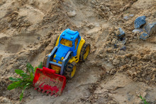 A Toy Tractor, Forgotten By A Child In The Sandbox. A Bright Plastic Toy Tractor. A Toy In The Playground. A Plaything Forgotten In The Sandbox. Forgotten Children's Plaything.