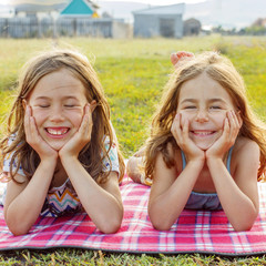 Two girls on picnic in a park on a plaid cute smile and look at the camera