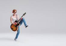 Young Woman Musician With An Acoustic Guitar In Hand On A Gray Background. He Laughs And Plays Rock And Roll Loudly. Full-length Portrait. On The Right There Is Space For Text