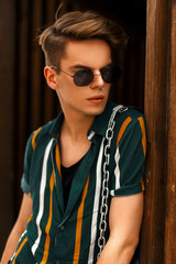 Wall Mural - Handsome young man with sunglasses in vintage colored shirt posing near a wooden wall